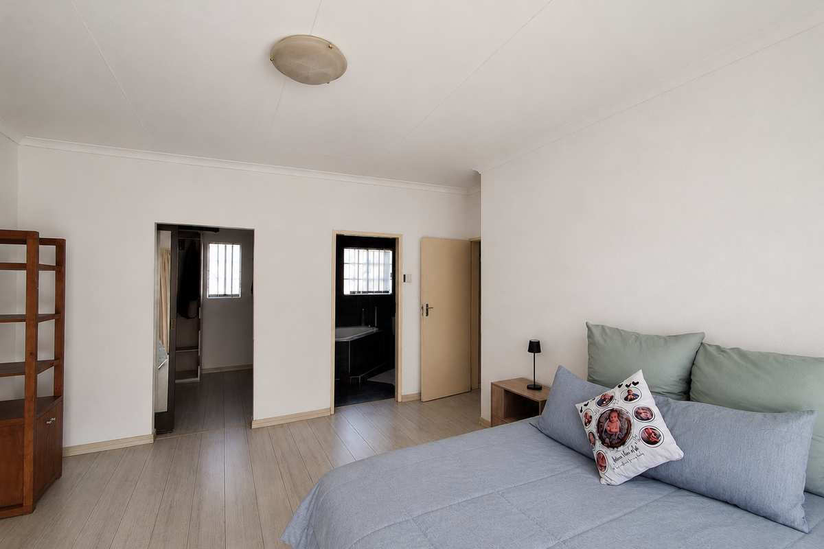 Spacious bedroom featuring light-toned laminate flooring, neutral walls, and direct access to an en-suite bathroom and walk-in closet area.