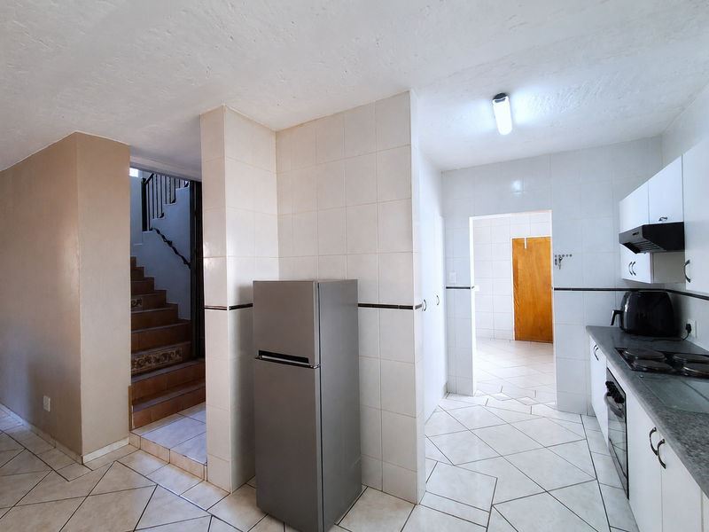 A functional kitchen area featuring tiled flooring, built-in cabinetry with integrated appliances, and an adjacent staircase leading to another level.