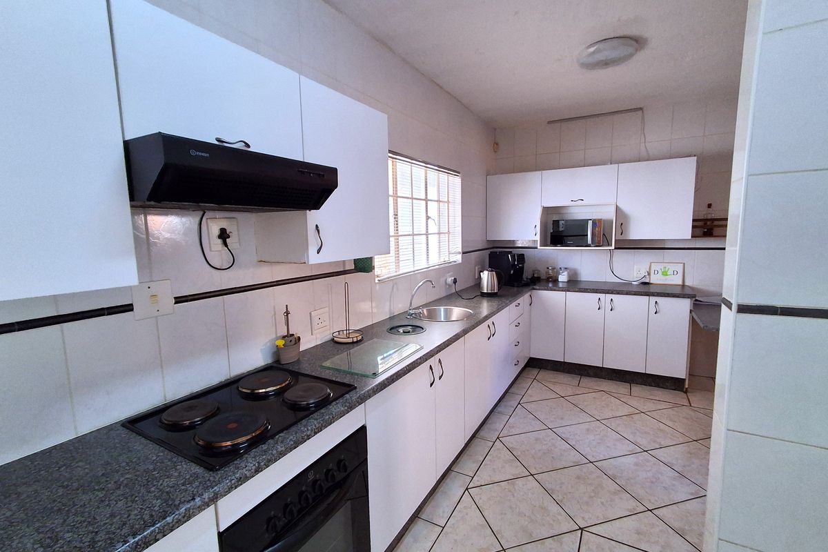 A functional kitchen featuring white cabinetry, dark laminate countertops, an electric hob, built-in oven, and tiled flooring with a neutral backsplash.