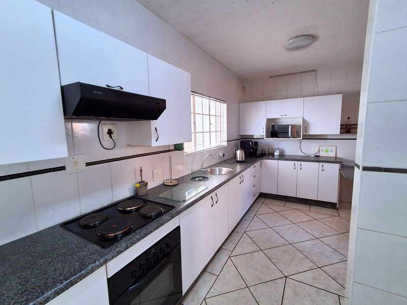 A functional kitchen featuring white cabinetry, dark laminate countertops, an electric hob, built-in oven, and tiled flooring with a neutral backsplash.