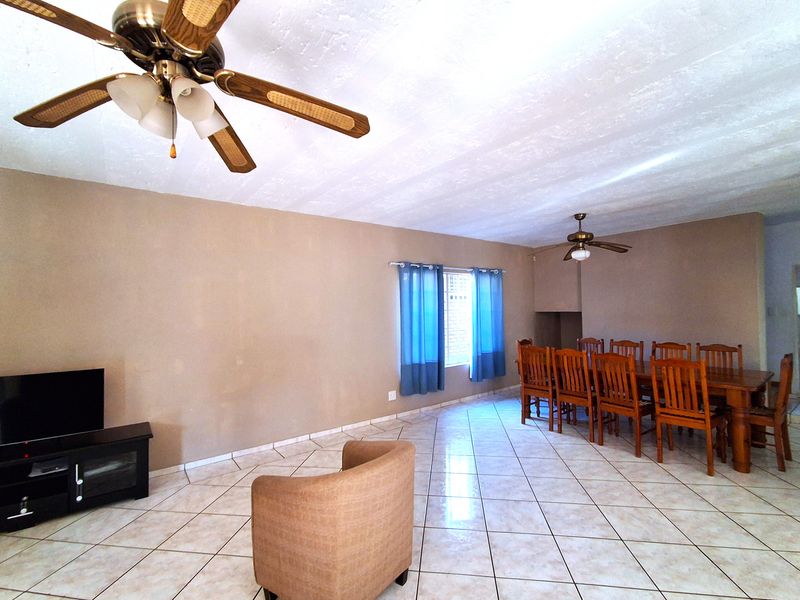 Spacious open-plan living and dining area featuring tiled flooring, dual ceiling fans, and natural light through a window with security bars.