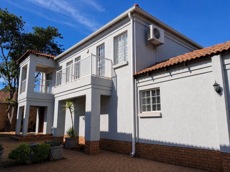 A well-maintained two-story rear elevation featuring a balcony with metal railings, terracotta roof tiles, and brick paving in the courtyard area.
