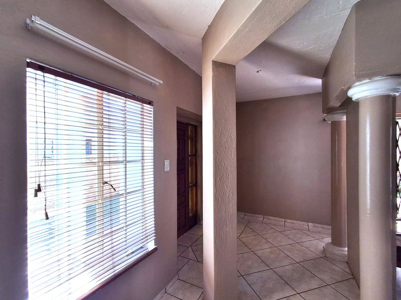 An empty hallway featuring tiled flooring, structural columns, and a timber door, providing a neutral canvas for interior design updates.
