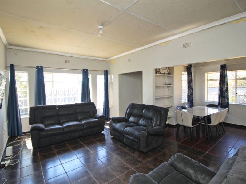 Open-plan living and dining area featuring dark tiled flooring, built-in shelving, and large windows, requiring cosmetic updates to the ceiling and wall finishes.