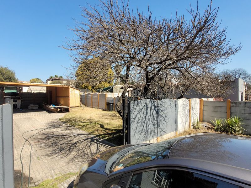 Rear yard area featuring a paved driveway, precast concrete boundary walling, and a covered storage structure.