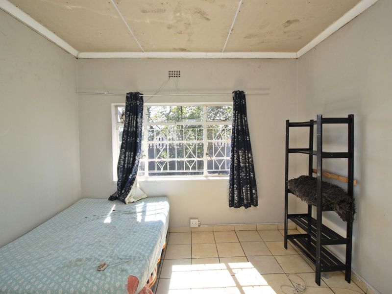A bedroom featuring tiled flooring and a window with security bars. The ceiling shows visible signs of staining and wear.