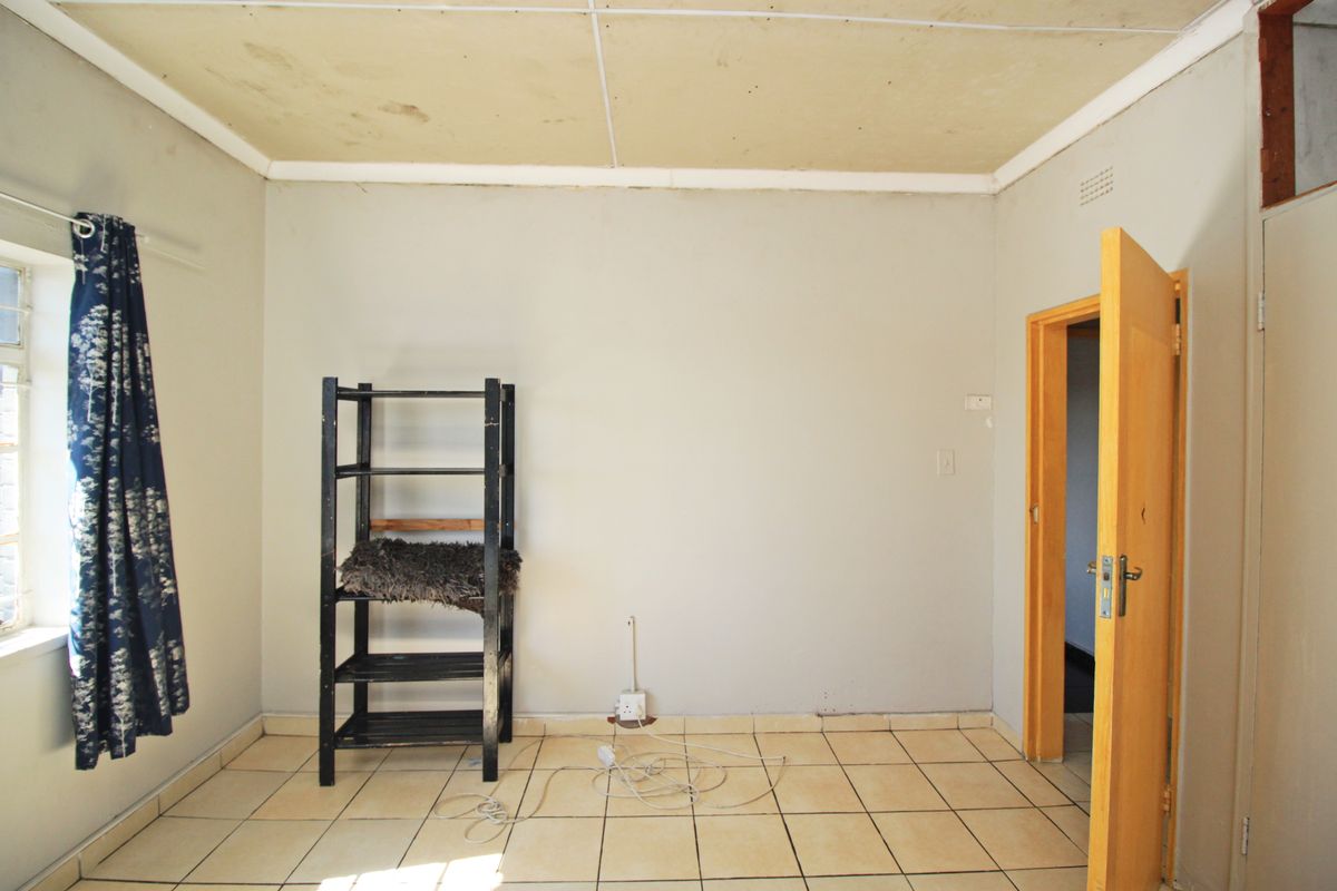 A vacant bedroom featuring tiled flooring and a timber door, requiring cosmetic updates to the ceiling and walls to improve its overall condition.