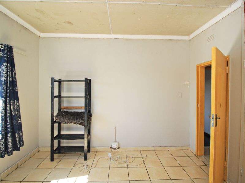 A vacant bedroom featuring tiled flooring and a timber door, requiring cosmetic updates to the ceiling and walls to improve its overall condition.