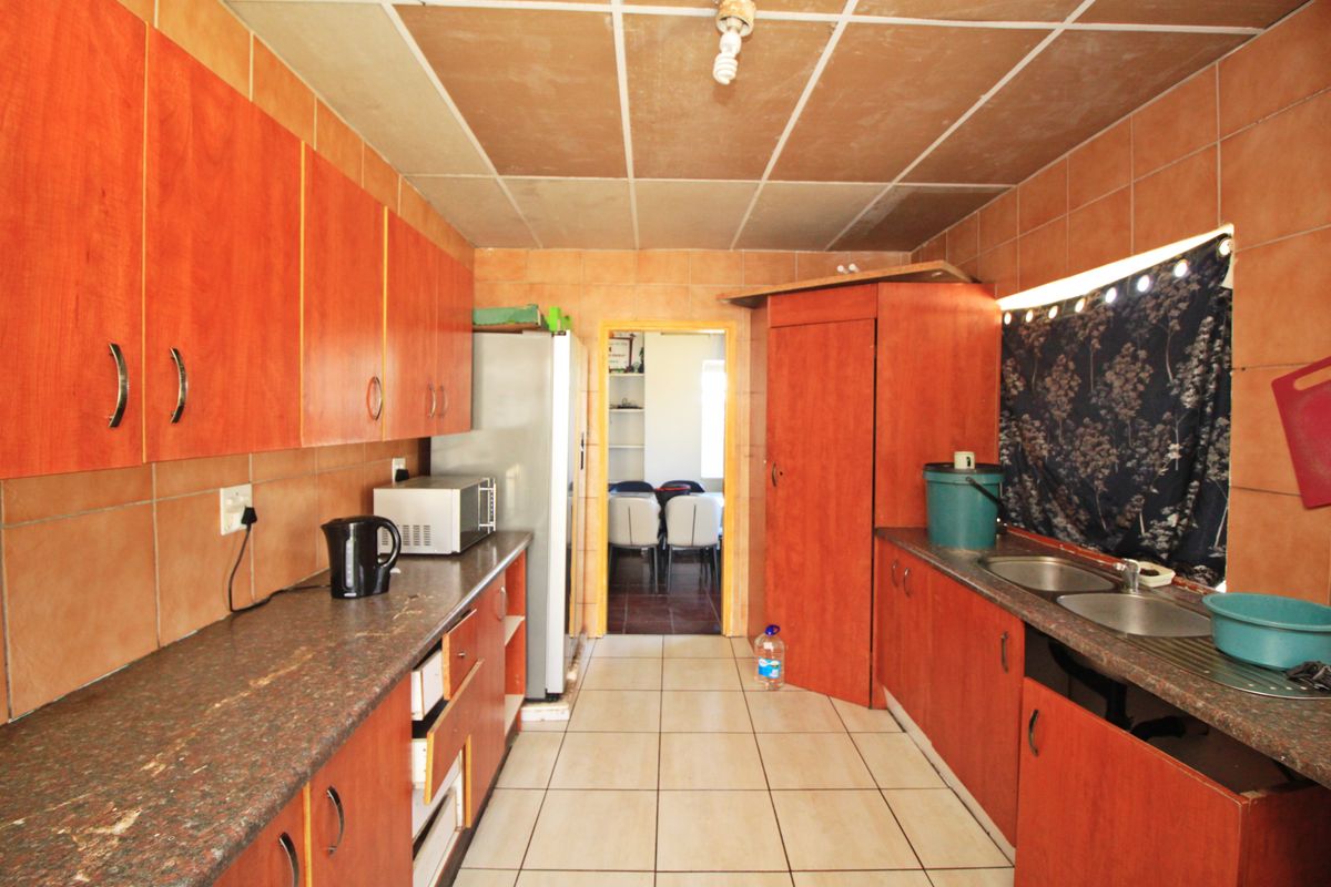 A functional kitchen featuring wood-look cabinetry, granite-style countertops, double stainless steel sink, and tiled finishes throughout.