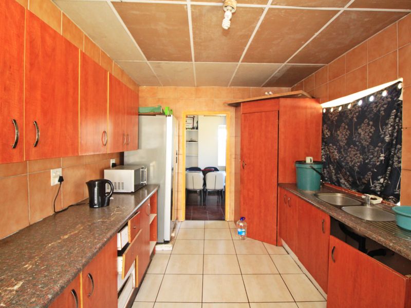 A functional kitchen featuring wood-look cabinetry, granite-style countertops, double stainless steel sink, and tiled finishes throughout.