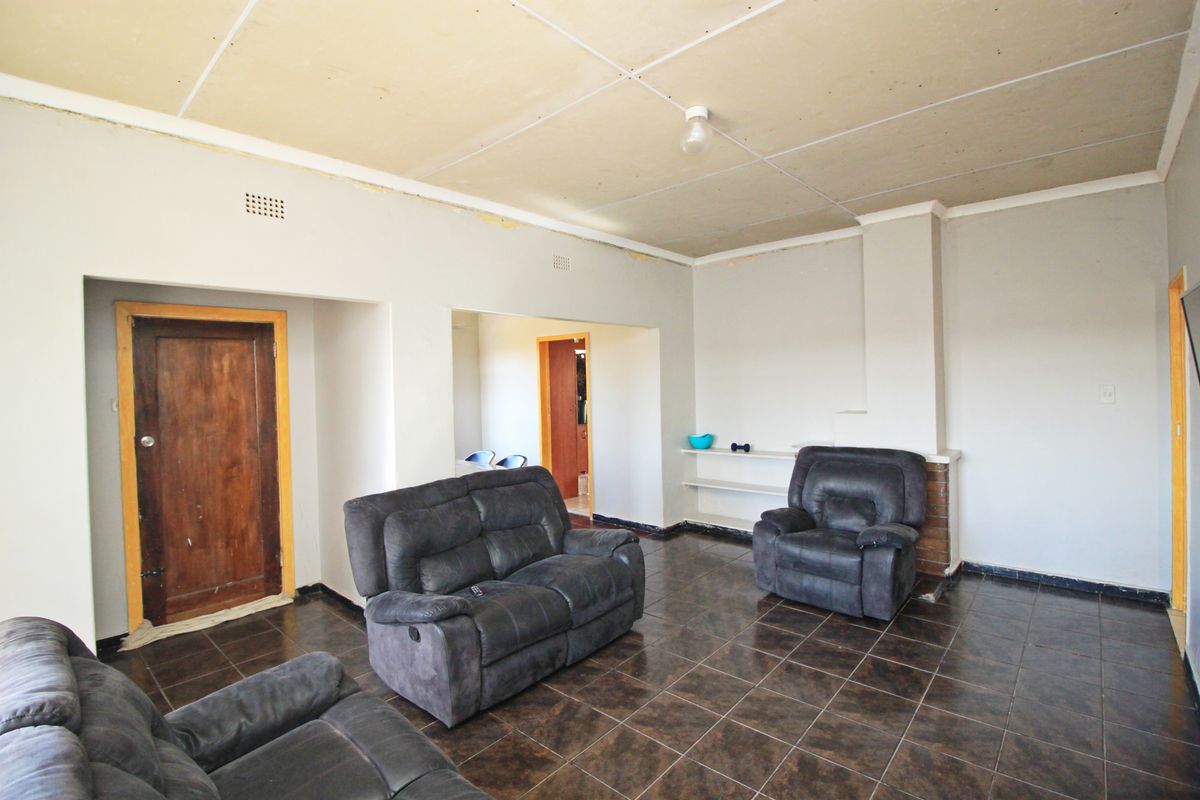 Spacious living room featuring dark tiled flooring, a brick fireplace surround, and built-in shelving, requiring ceiling and trim finishing to complete the space.
