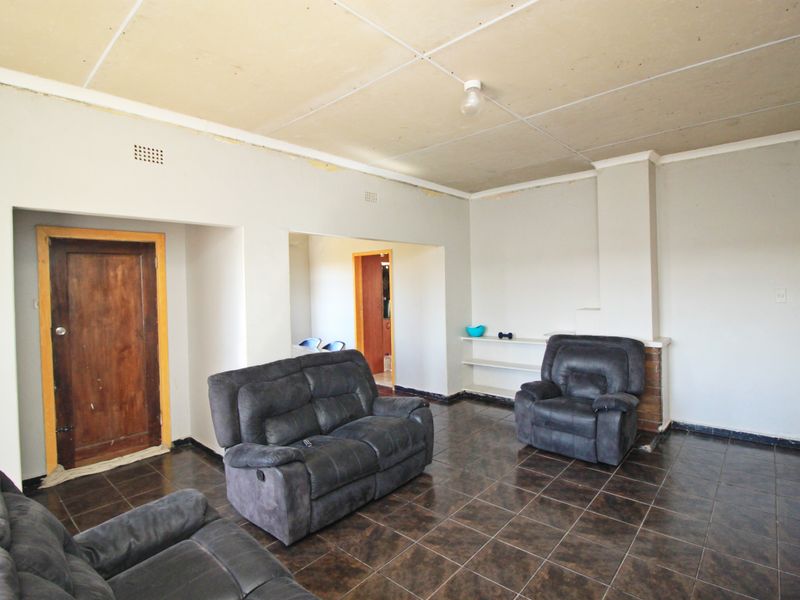 Spacious living room featuring dark tiled flooring, a brick fireplace surround, and built-in shelving, requiring ceiling and trim finishing to complete the space.