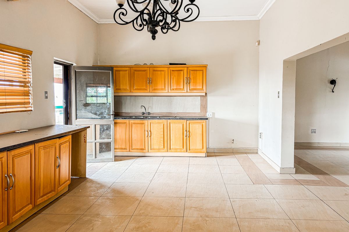 A spacious kitchen featuring wooden cabinetry, tiled flooring, and an integrated sink, offering a functional layout ready for modern updates.