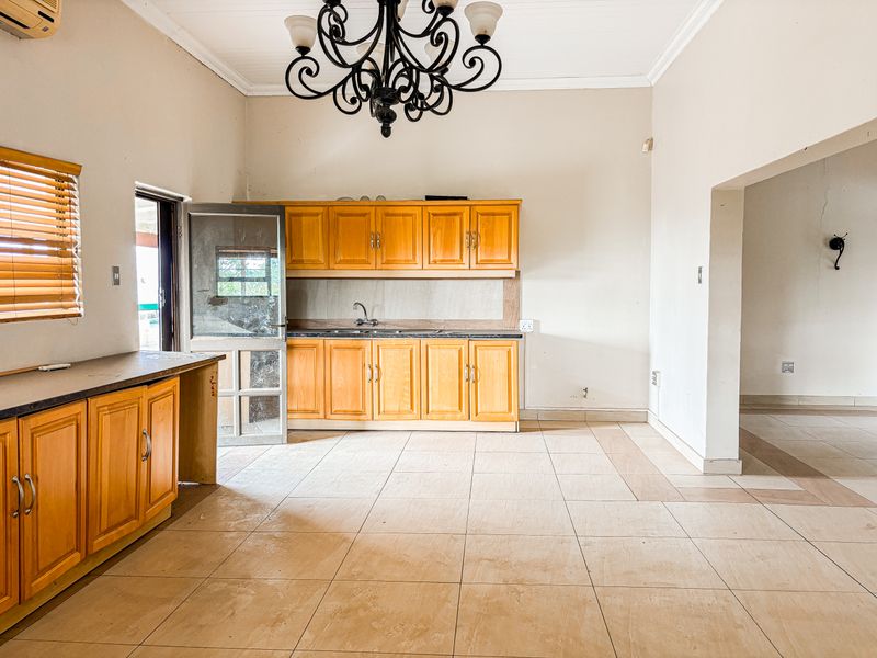 A spacious kitchen featuring wooden cabinetry, tiled flooring, and an integrated sink, offering a functional layout ready for modern updates.