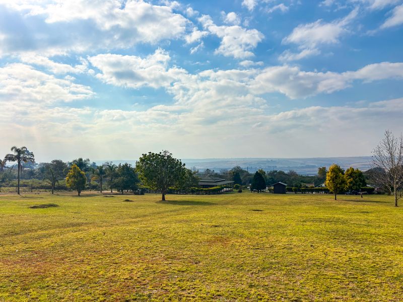 A wide-angle view of a spacious, well-maintained garden featuring expansive green lawns and mature trees under a bright, cloudy sky.