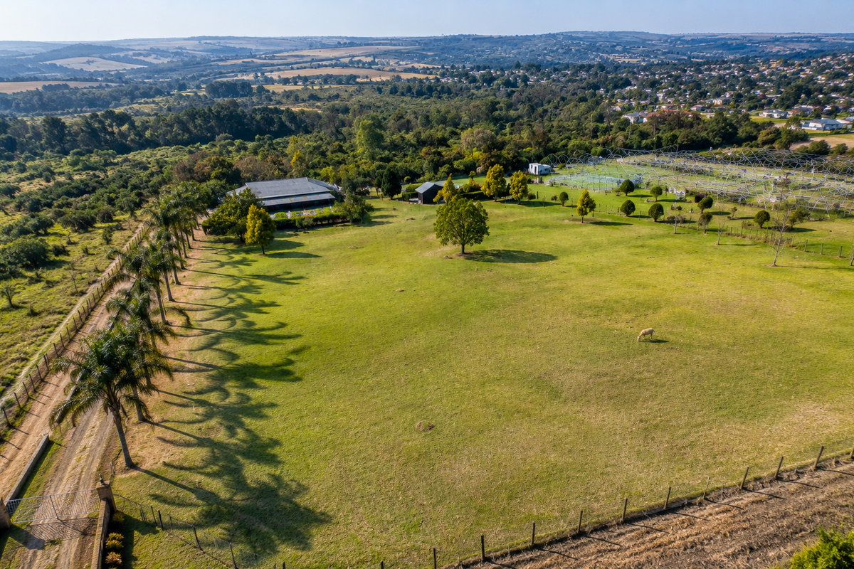 An expansive aerial view of a large property featuring extensive green lawns, mature trees, a driveway, and a rural landscape setting.