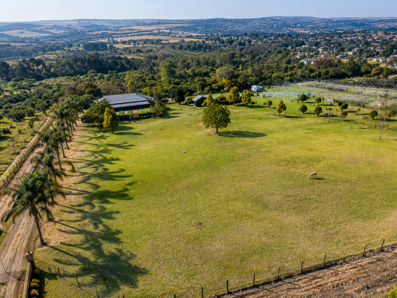 An expansive aerial view of a large property featuring extensive green lawns, mature trees, a driveway, and a rural landscape setting.
