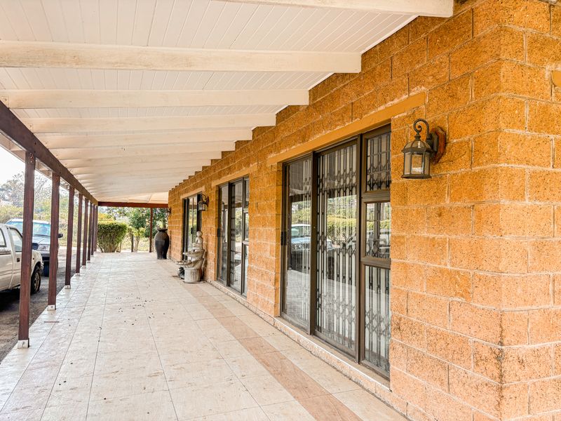 A spacious covered patio featuring exposed brick walls, tiled flooring, and sliding glass doors with security gates, providing a functional outdoor transition space.