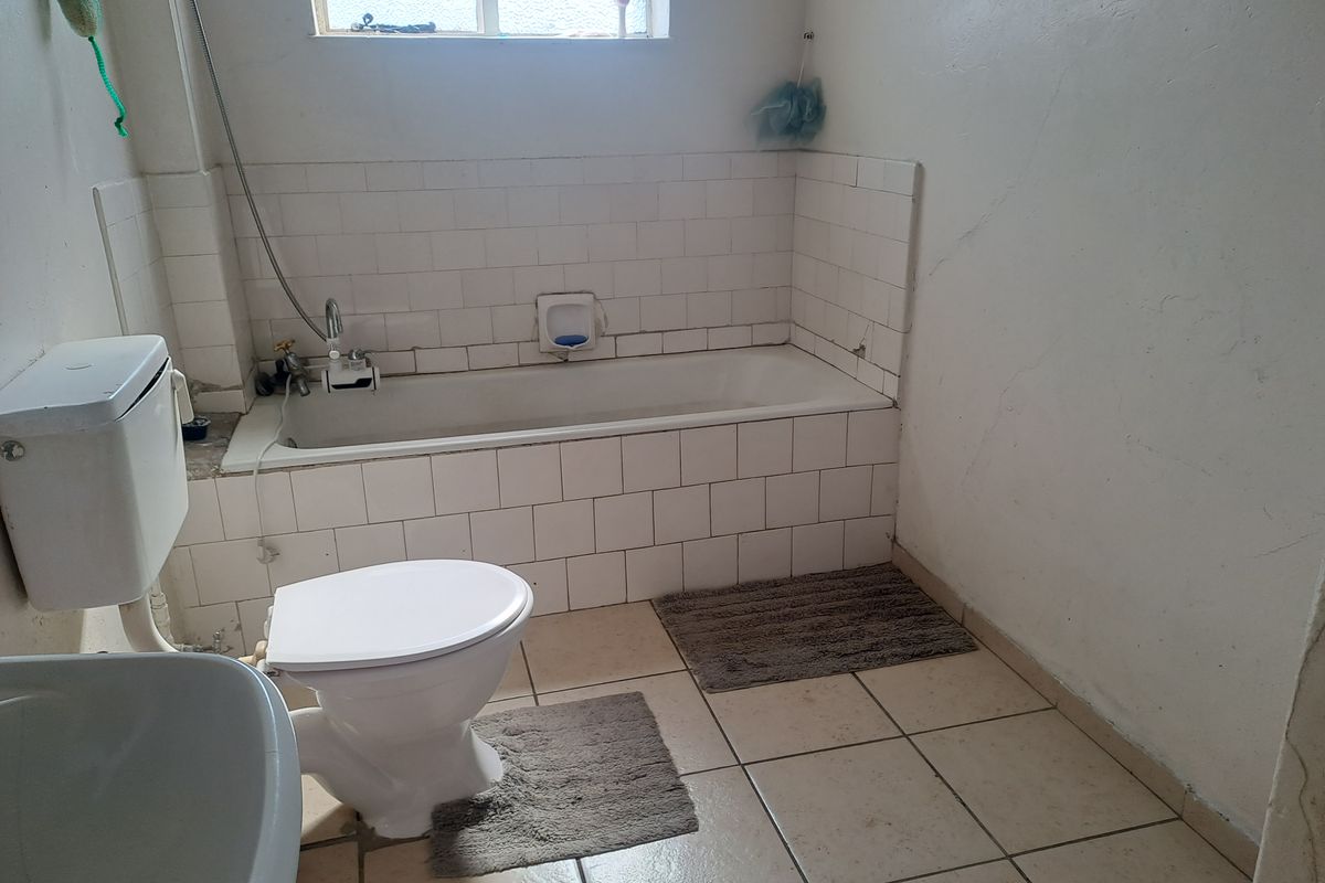 A functional bathroom featuring a bathtub, toilet, and tiled finishes, currently requiring cosmetic updates and maintenance to improve its overall condition.