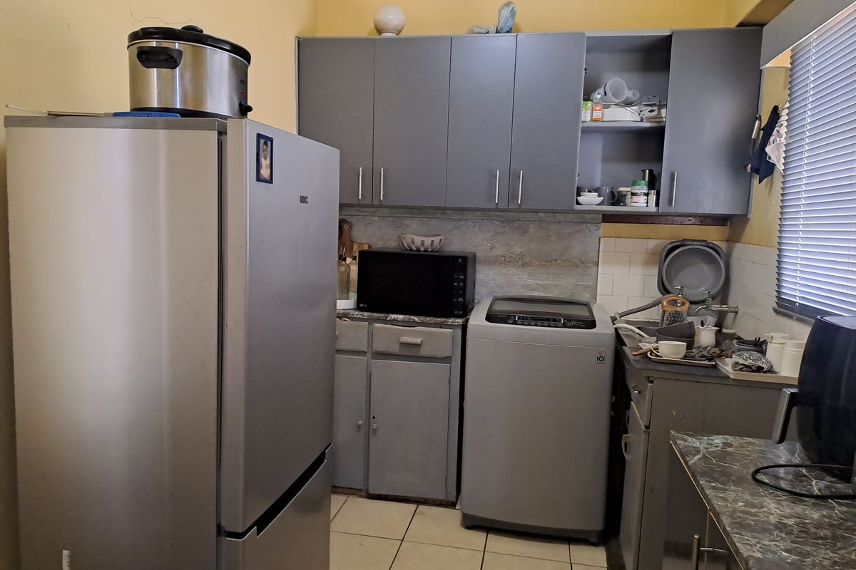 A compact kitchen featuring grey built-in cabinetry, tiled backsplash, and tiled flooring, requiring some cosmetic updates to improve its overall condition.
