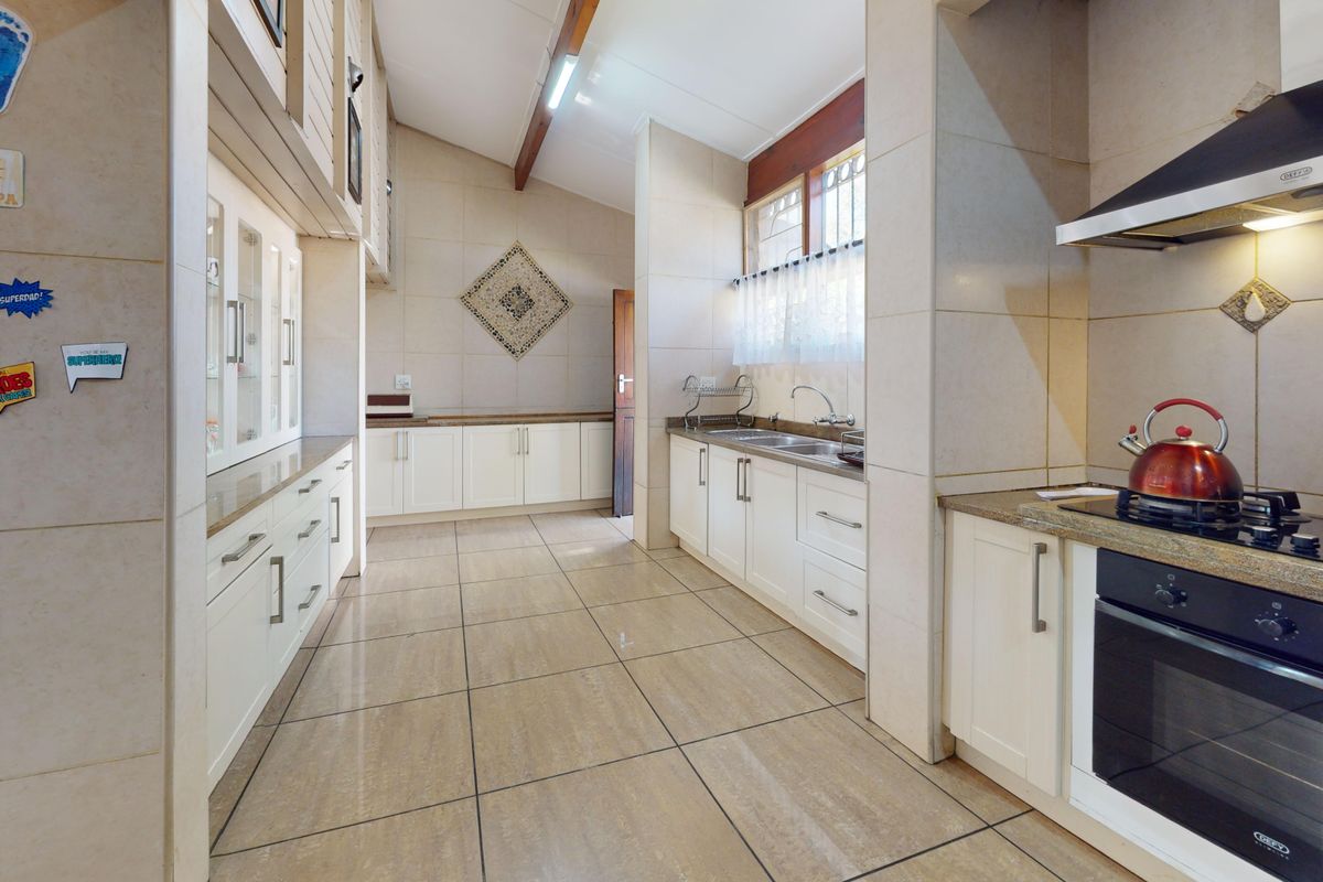 A well-maintained kitchen featuring white cabinetry, granite countertops, built-in oven, gas hob, extractor fan, and tiled flooring with exposed timber ceiling beams.