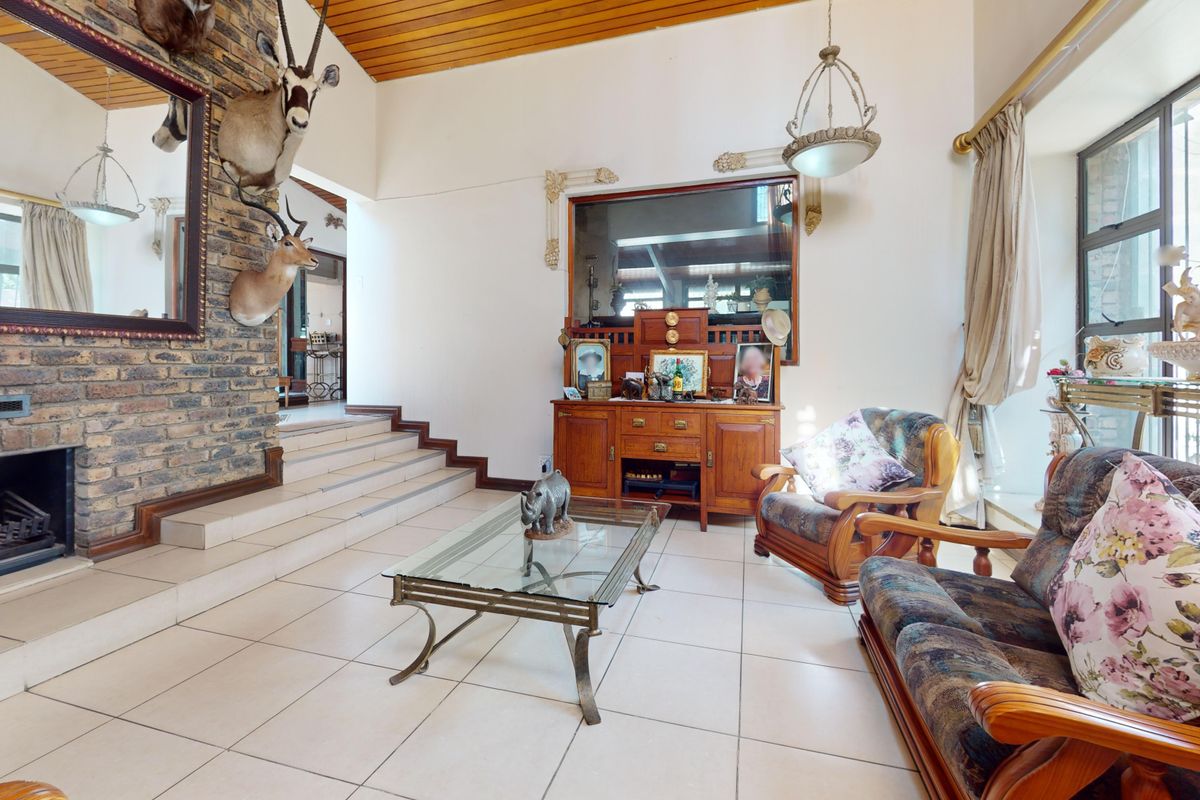 Spacious living room featuring a prominent brick fireplace, timber-clad ceiling, and tiled flooring, with a raised platform leading to adjacent areas.