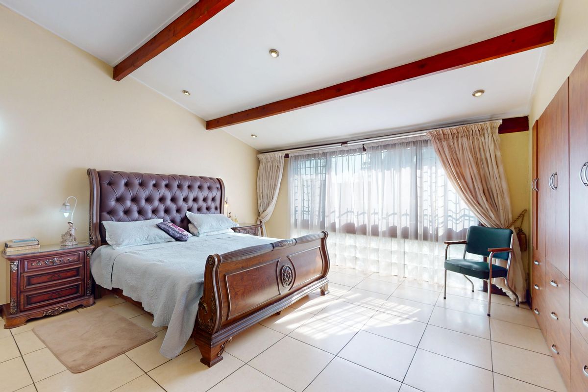 Spacious bedroom featuring exposed timber ceiling beams, tiled flooring, and extensive built-in cupboard storage with natural light from large windows.