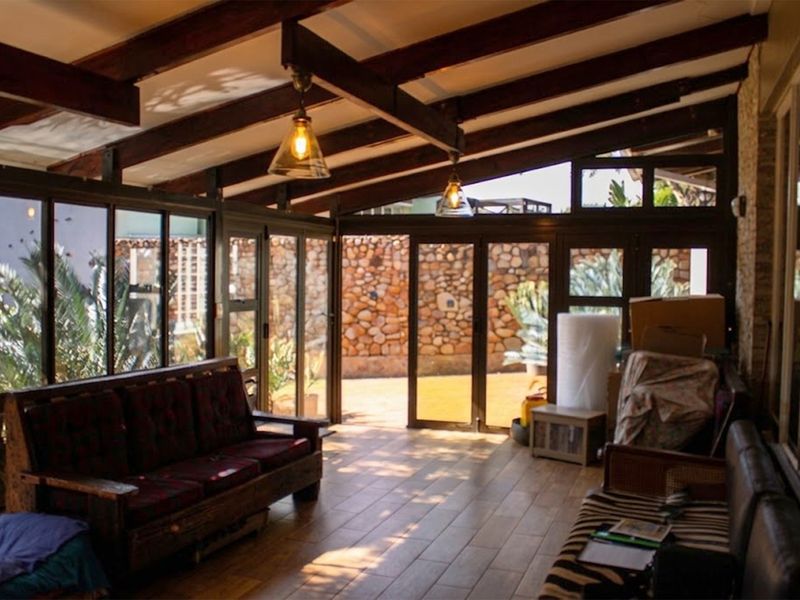 A bright, enclosed patio featuring exposed timber beams, tiled flooring, and large glass doors opening to a stone-walled garden area.