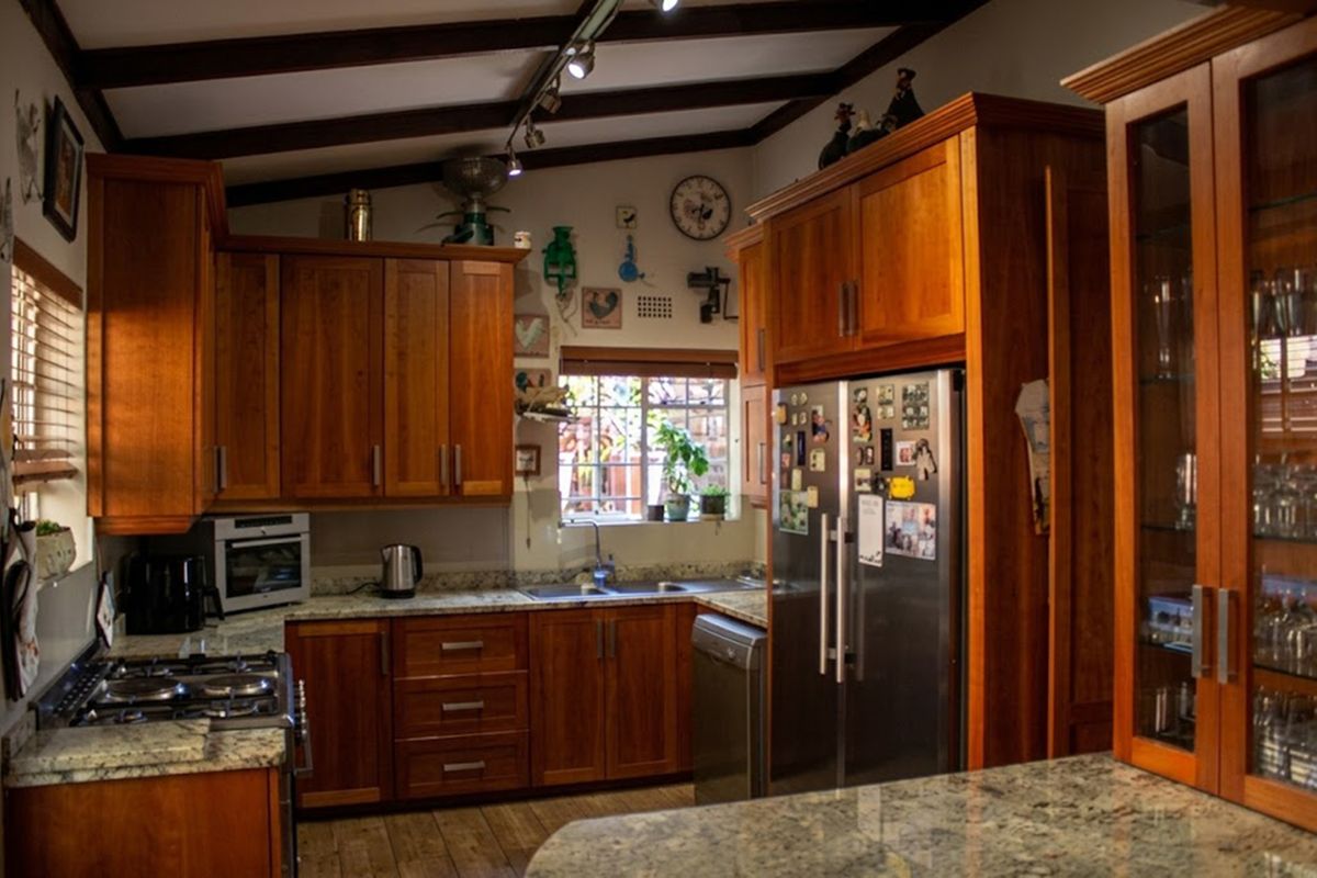 A warm, traditional kitchen featuring rich wooden cabinetry, granite countertops, exposed ceiling beams, and integrated appliances, offering a functional and inviting cooking space.