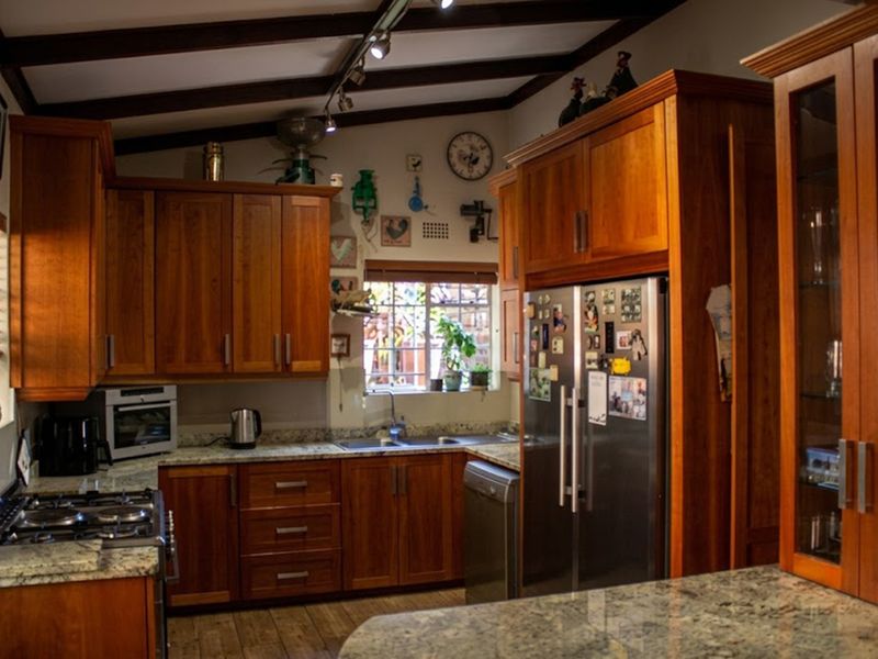 A warm, traditional kitchen featuring rich wooden cabinetry, granite countertops, exposed ceiling beams, and integrated appliances, offering a functional and inviting cooking space.