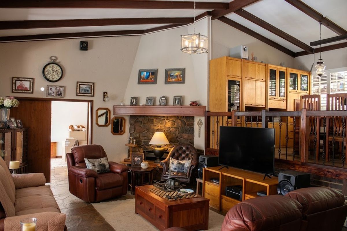 Spacious living room featuring a stone fireplace, exposed timber ceiling beams, and built-in cabinetry with a raised dining area transition.