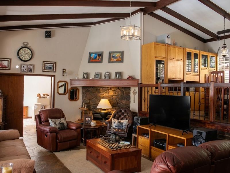 Spacious living room featuring a stone fireplace, exposed timber ceiling beams, and built-in cabinetry with a raised dining area transition.