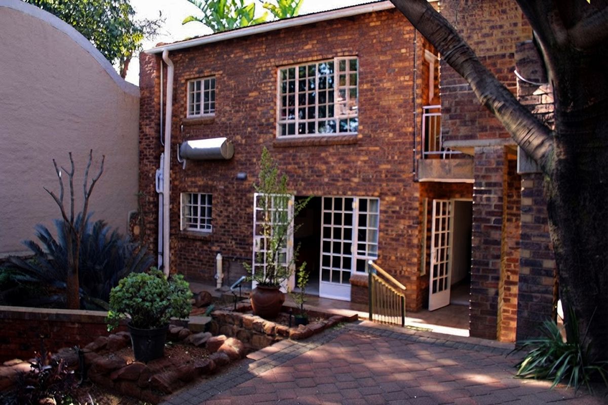 Rear view of a two-story exposed brick house featuring a paved patio area, multiple french doors, and a solar water heating system.