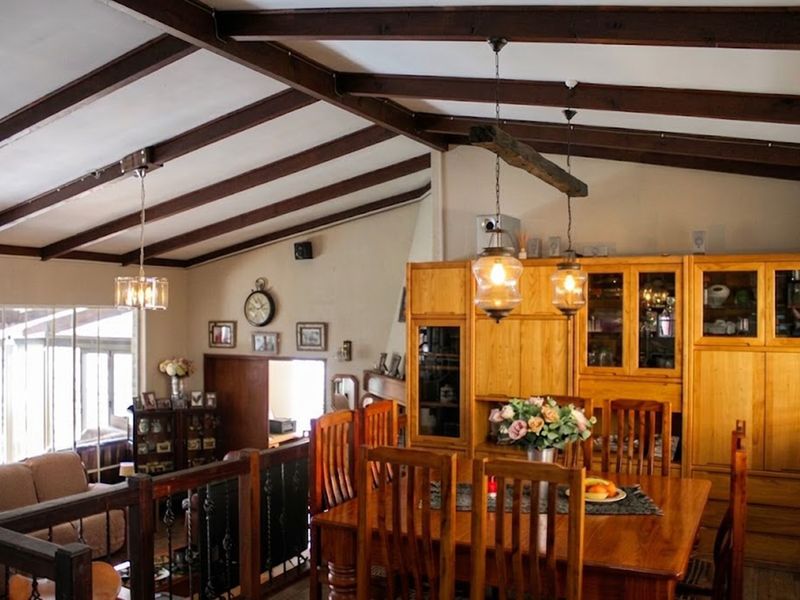 Spacious open-plan living and dining area featuring vaulted ceilings with exposed timber beams, built-in wooden cabinetry, and a decorative wrought iron balustrade.