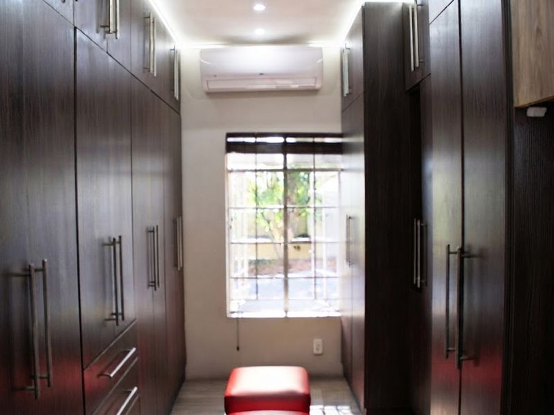 A walk-in closet or dressing area featuring extensive dark wood built-in cabinetry, a split-system air conditioner, and a window with security bars.