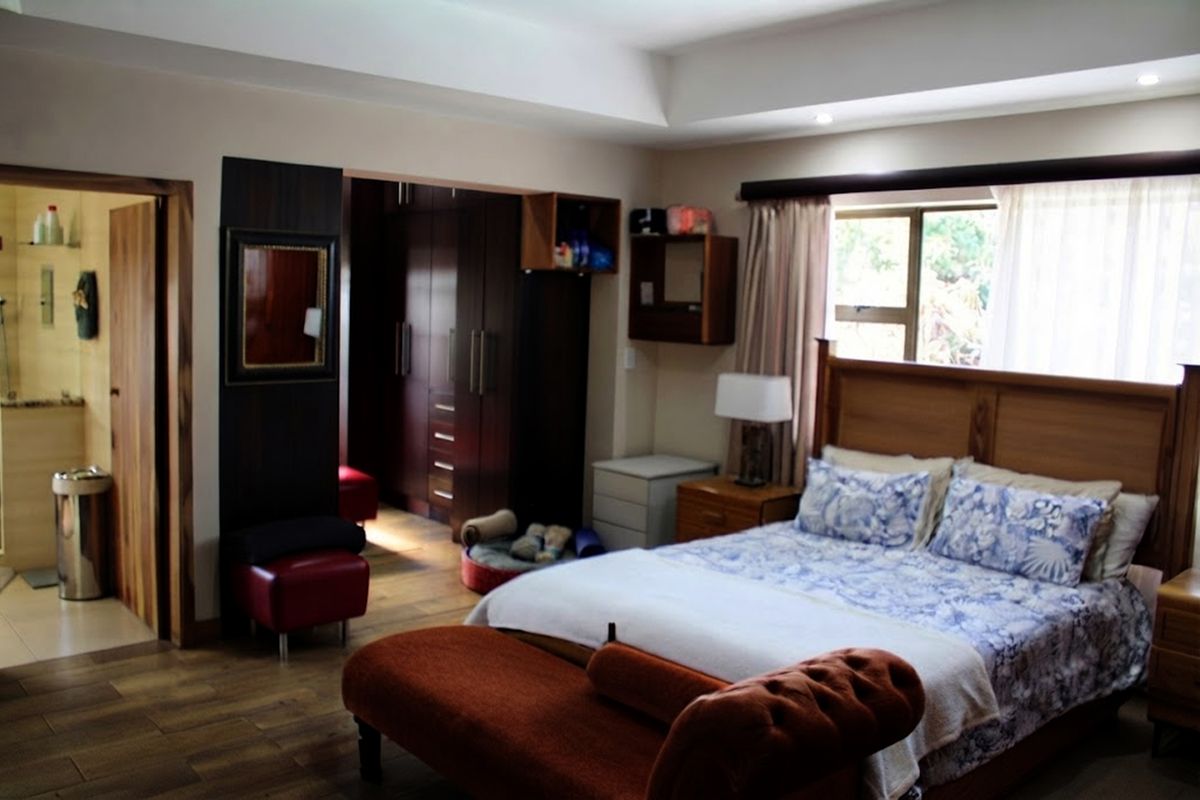 Spacious bedroom featuring built-in cupboards, a recessed ceiling, and an adjoining en-suite bathroom with tiled flooring throughout.