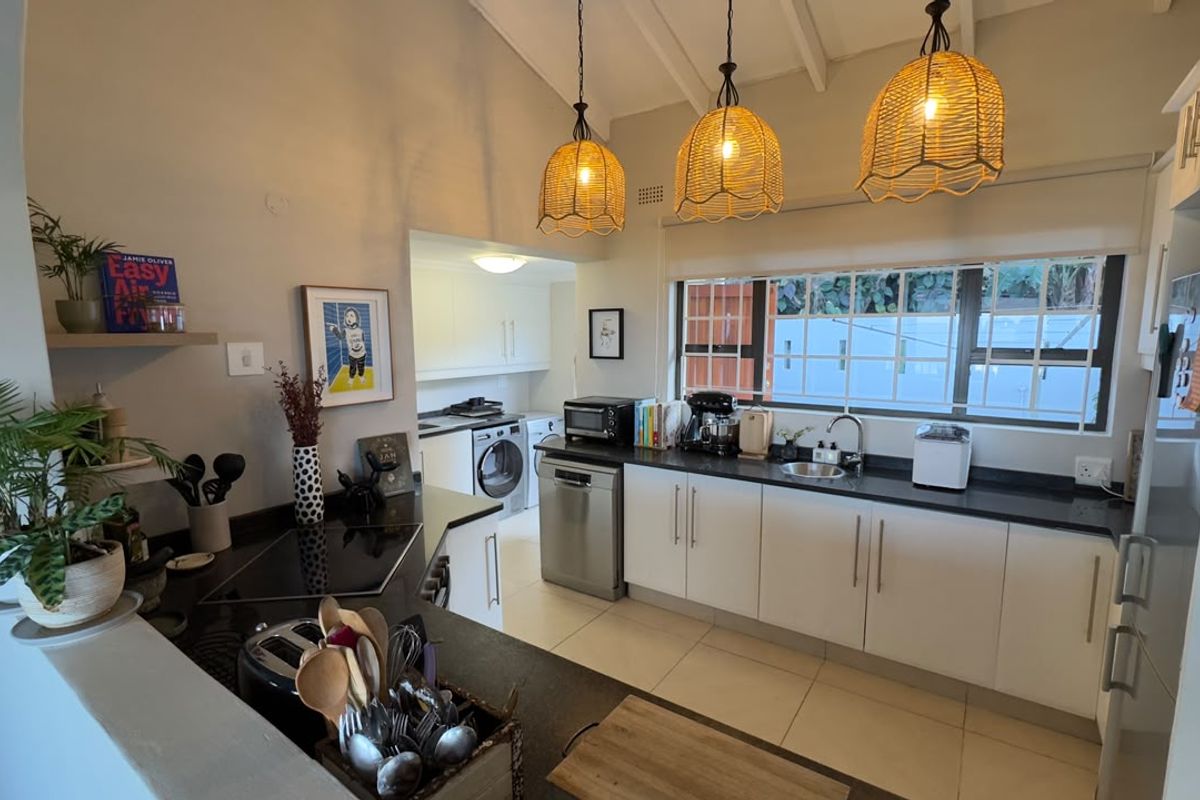 A bright, modern kitchen featuring white cabinetry, dark stone countertops, vaulted ceilings, and a functional layout with an adjacent laundry area.
