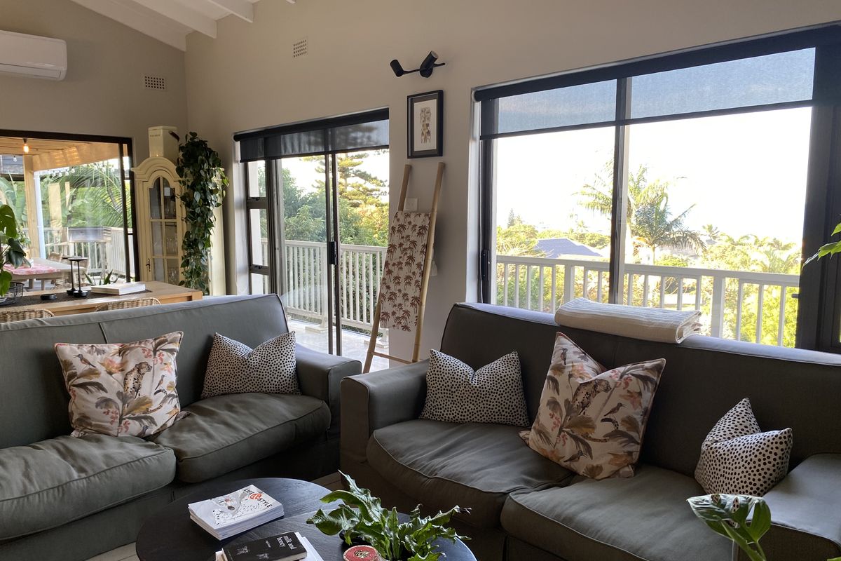 Spacious living room featuring vaulted ceilings with exposed rafters, large sliding glass doors providing natural light, and direct access to an outdoor balcony area.