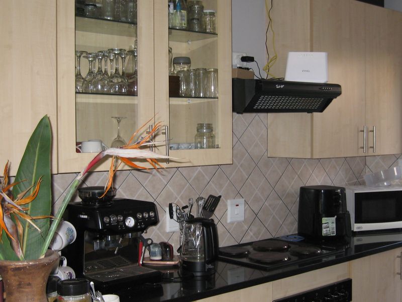 A functional kitchen featuring light wood cabinetry, black granite countertops, a tiled backsplash, and a built-in electric hob with an extractor fan.