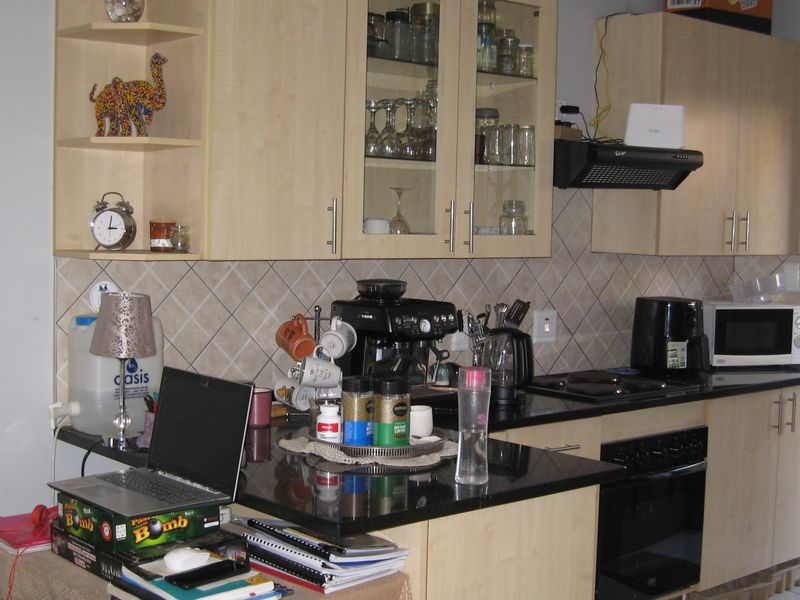 Functional kitchen featuring light-wood cabinetry, black granite countertops, built-in oven, electric hob, and a tiled backsplash.