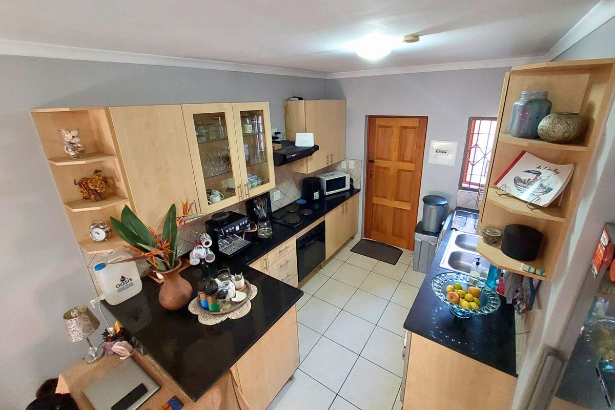 A functional kitchen featuring light wood cabinetry, dark granite countertops, a double basin sink, and built-in cooking appliances with tiled flooring.