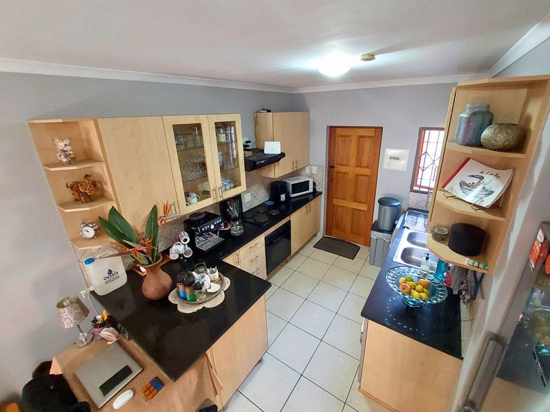 A functional kitchen featuring light wood cabinetry, dark granite countertops, a double basin sink, and built-in cooking appliances with tiled flooring.