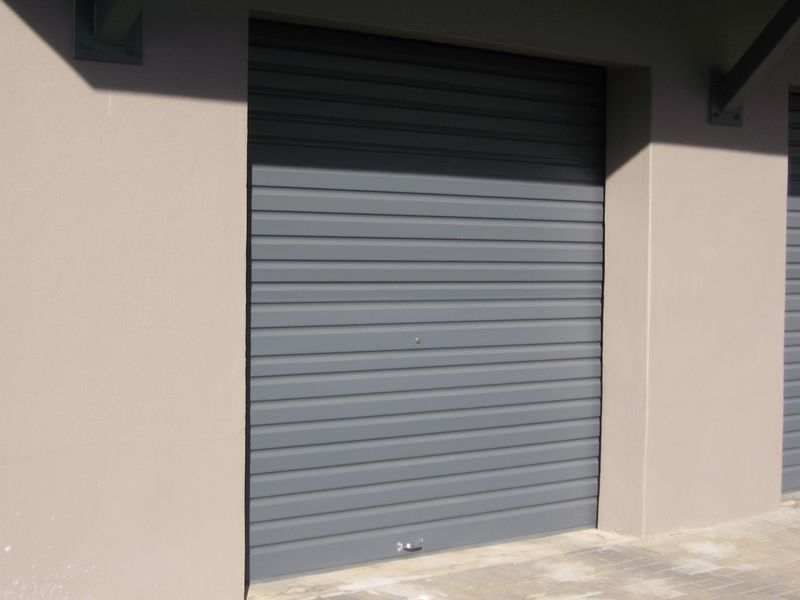 A secure, grey roller shutter garage door set within a neutral-toned exterior wall, featuring a clean paved approach.