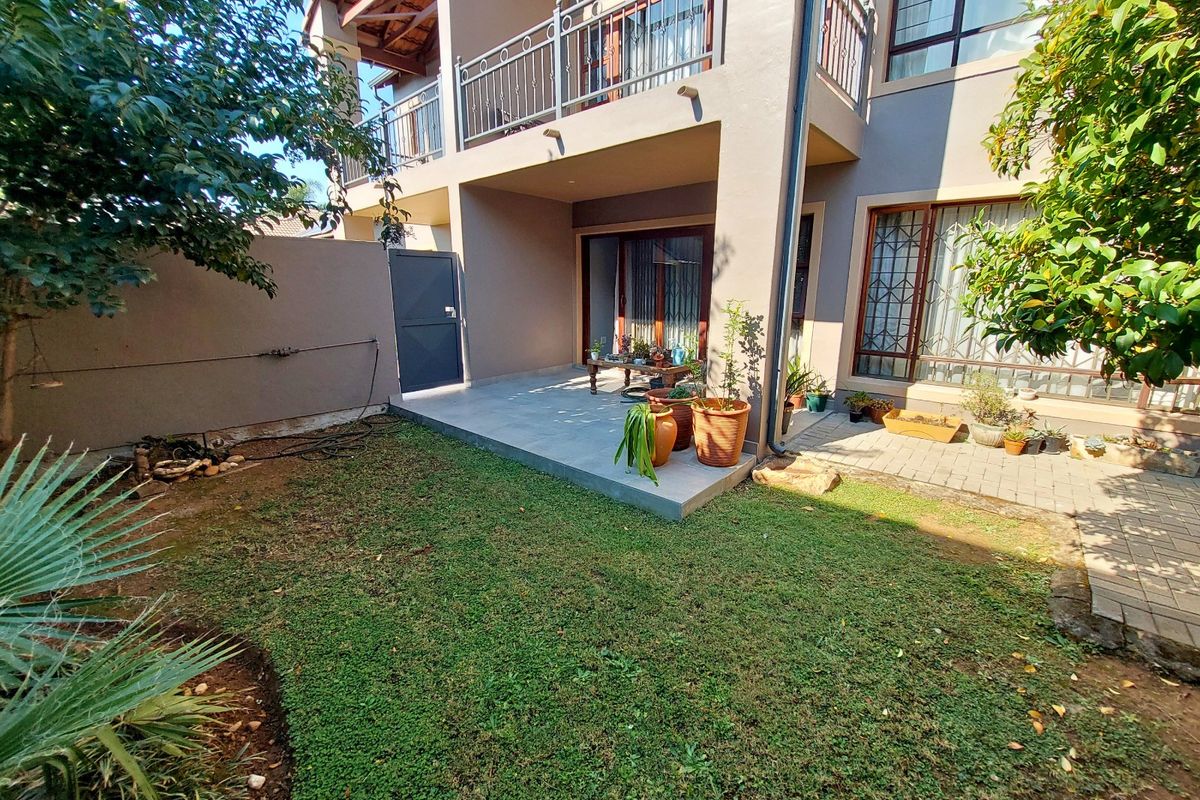 Rear view of the townhouse featuring a paved patio area, a small garden, and an upper-level balcony with metal railings.