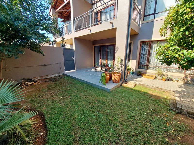 Rear view of the townhouse featuring a paved patio area, a small garden, and an upper-level balcony with metal railings.