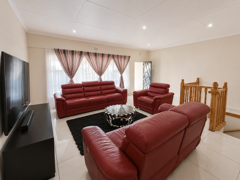 Spacious living room featuring neutral tiled flooring, recessed downlighting, and a wooden staircase balustrade, providing a bright and open atmosphere.