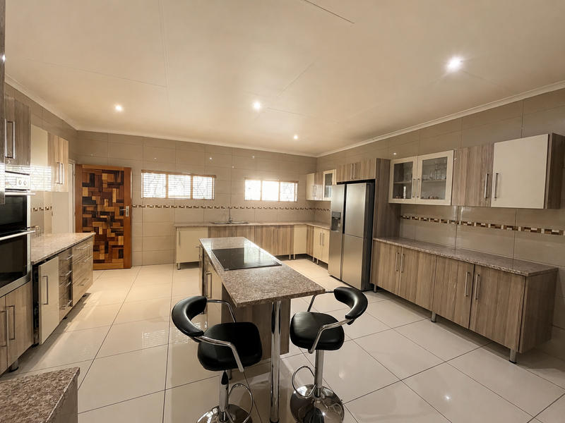 Modern kitchen featuring extensive built-in cabinetry, granite countertops, a central island with a built-in hob, and high-gloss tiled flooring.