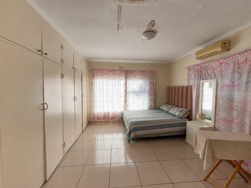 Spacious bedroom featuring extensive built-in cupboards, tiled flooring, and an air conditioning unit, though the ceiling requires repair due to visible water damage.