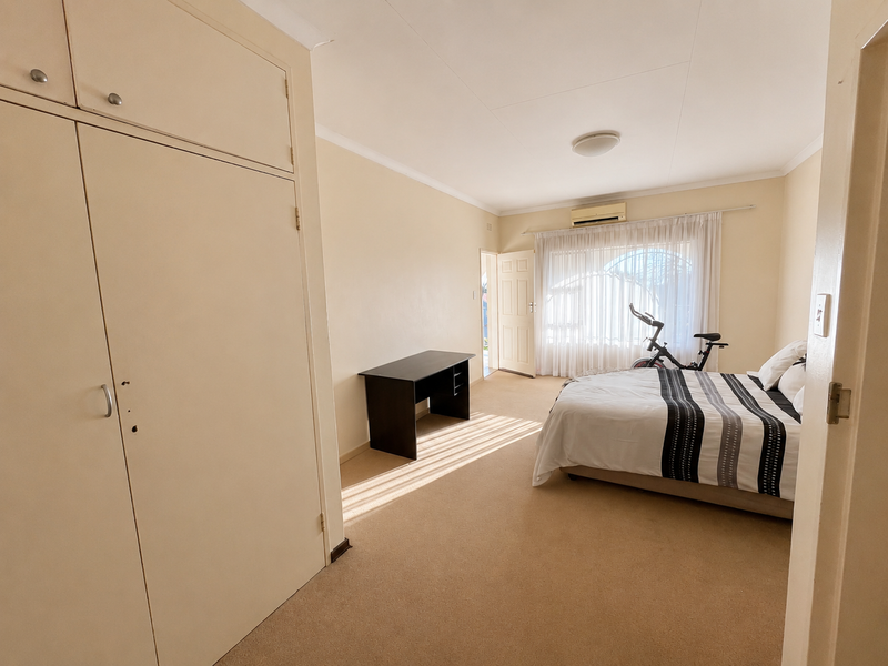 A spacious bedroom featuring built-in cupboards, wall-to-wall carpeting, and a wall-mounted air conditioning unit, offering a functional and neutral living space.
