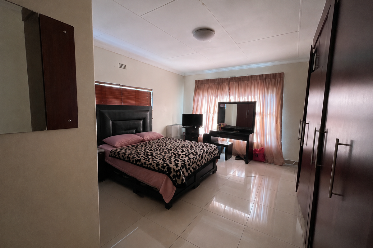 Spacious bedroom featuring tiled flooring, built-in cupboards, and large windows with curtains. Note visible water staining on the ceiling.